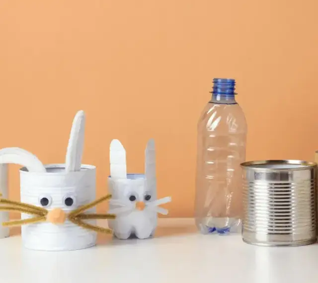 Zające z rolek po papierze i puszek to świetne przykłady recyklingu w życiu codziennym. W tle pusta butelka i rolka po ręczniku papierowym.
