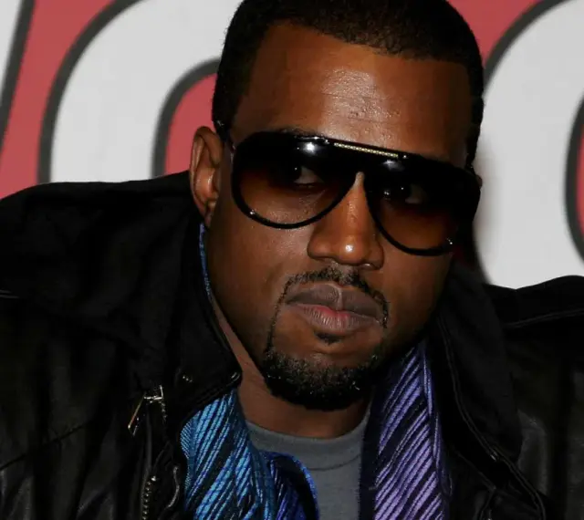 Kanye West w okularach przeciwsłonecznych i skórzanej kurtce, gotowy na koncert w Polsce.
