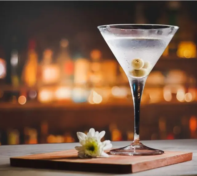Kieliszek martini z oliwkami i kwiatkiem na blacie. Idealny dodatek do drinka, by wiedzieć, z czym pić martini.