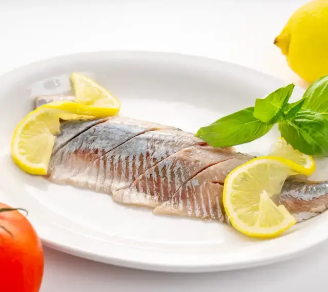 Filety śledzi z cytryną i bazylią na talerzu. Kto nie powinien jeść śledzi? Alergicy i osoby z problemami z cholesterolem.