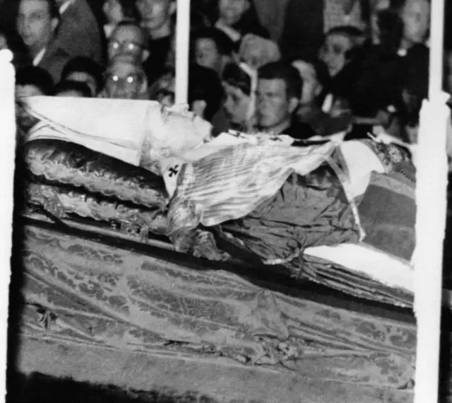 Pius XII w szatach, przygotowany do balsamowania. Tłum ludzi w tle.