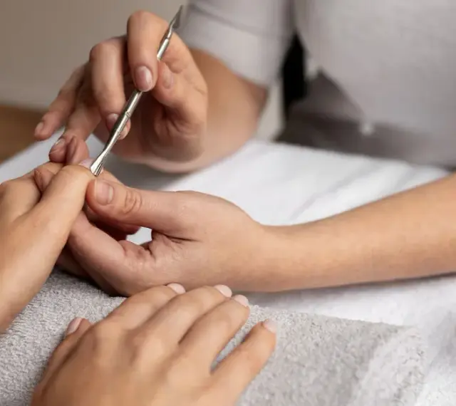 Profesjonalny manicure kombinowany w toku. Dłonie są zadbane, a kosmetyczka precyzyjnie pracuje narzędziami.