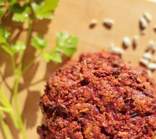 Pyszne kotlety z buraka, przypominające falafel, leżą na desce obok gałązki pietruszki i nasion słonecznika.