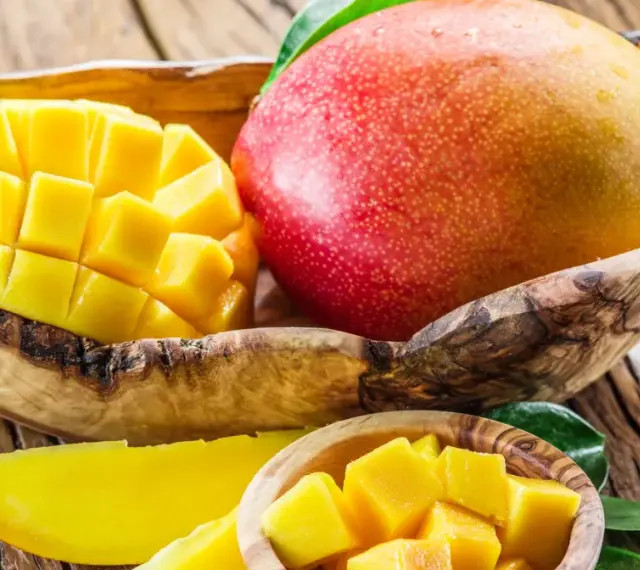 Soczyste, pokrojone w kostkę i w całości mango w drewnianej misce. Owoc ten zawiera mnóstwo witamin.