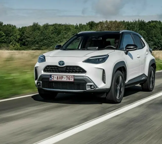 Biały Yaris Cross Hybrid jedzie po drodze, otoczony zielenią.