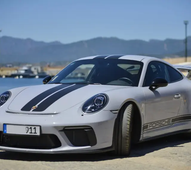 Szary Porsche 911 z czarnymi pasami, stojący nad wodą. Zastanawiasz się nad porsche 911 cena?