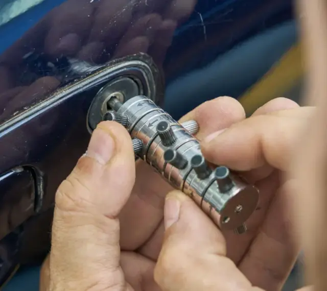 Specjalista manipuluje zamkiem, by otworzyć auto. Dowiedz się, ile kosztuje awaryjne otwieranie samochodu.