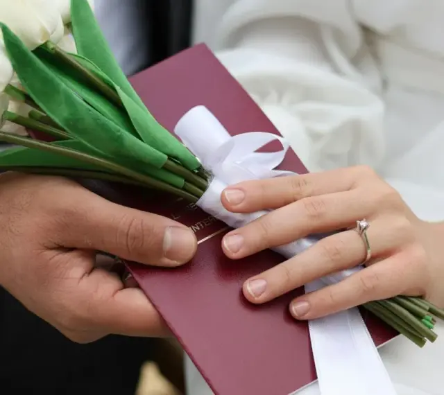 Para weselna trzyma bukiet białych tulipanów i akt małżeństwa. Zastanawiasz się, ile się daje na wesele?