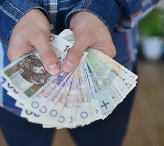 Dłonie trzymające plik polskich banknotów. Czy to zapłata za coś, czy może przyszła renta alkoholowa?