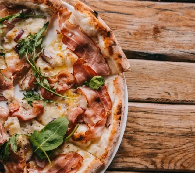 Pyszna pizza carbonara z chrupiącym boczkiem, rukolą i cebulą na drewnianym stole.