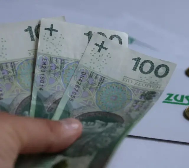 Trzy stuzłotowe banknoty w dłoni, obok dokument ZUS i monety. Czy to zapowiedź 30 krotności ZUS 2025?