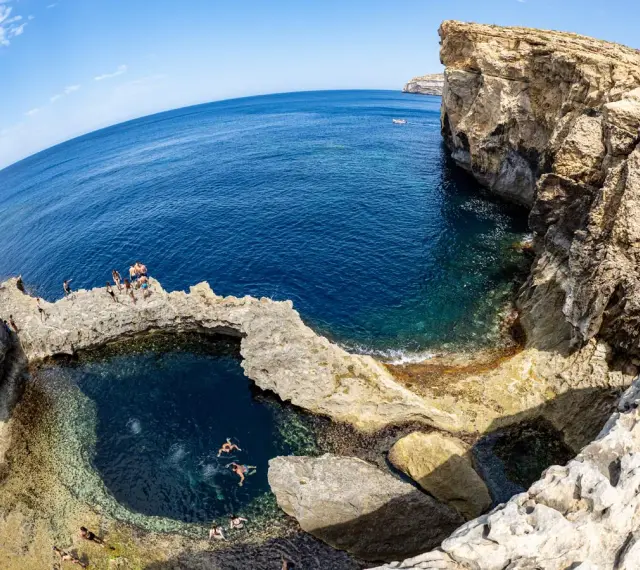Ludzie kąpią się w naturalnym basenie skalnym, znanym jako blue hole, otoczonym klifami i turkusowym morzem.