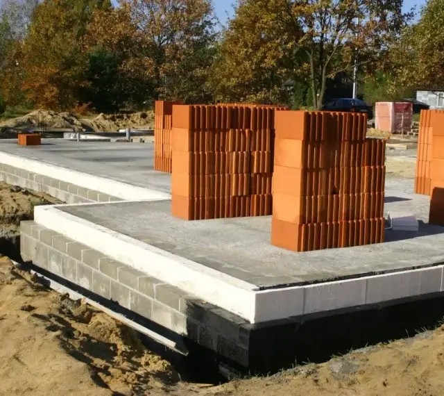 Budowa domu: fundamenty z bloczków betonowych, płyta fundamentowa i stosy pustaków ceramicznych.