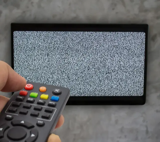 Ręka trzyma pilot dekodera, celując w ekran telewizora z zakłóceniami. Czas na naukę, jak sparować pilot dekodera z telewizorem.