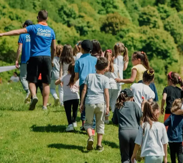 Un groupe d'enfants suit un coach sur une colline verdoyante. Ces actions pour financer un voyage scolaire sont pleines d'énergie et de joie.