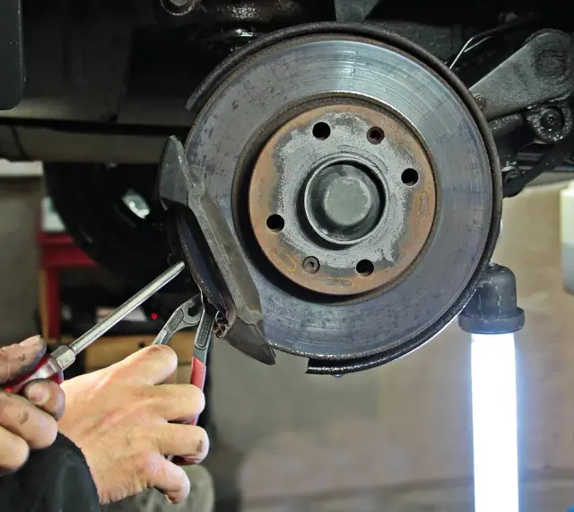 Dłonie mechanika z narzędziami przy hamulcu tarczowym samochodu.