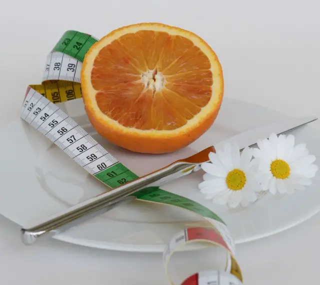 Pomarańcza na talerzu z miarką krawiecką i kwiatami symbolizuje zdrową dietę odchudzającą.