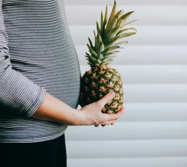 Brzuch kobiety w paski, trzymająca ananasa. Wygląda jak ananas w ciąży, symbolizujący zdrową dietę.