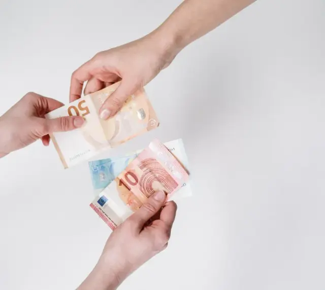 Dwie dłonie przekazują sobie banknoty euro. W Hiszpanii obowiązuje euro, więc to właśnie ta waluta jest tu widoczna.