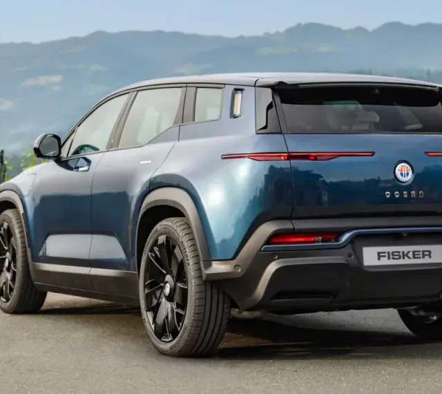 Tylna część niebieskiego elektrycznego SUV-a Fisker Ocean na tle gór i zieleni.
