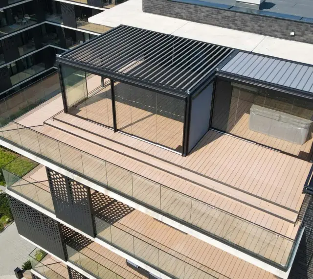 Nowoczesny taras na dachu z przeszklonym pawilonem i pergolą. Drewniana podłoga i szklane balustrady tworzą elegancką przestrzeń.