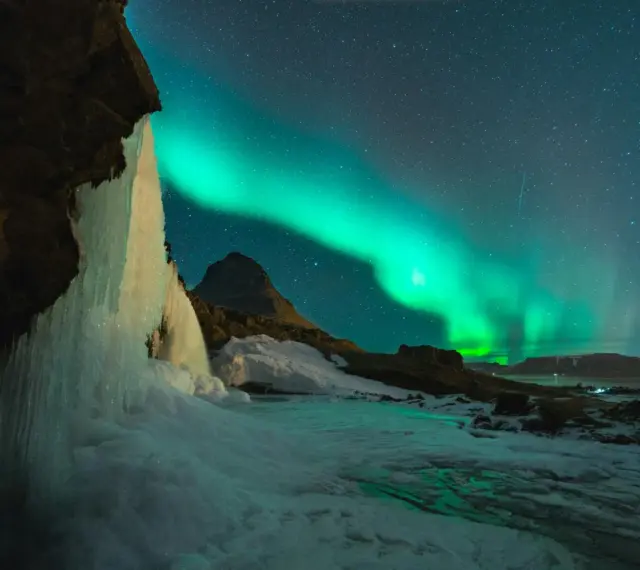 Lodowy wodospad i zorza polarna na nocnym niebie. Islandia w styczniu, magiczny widok.