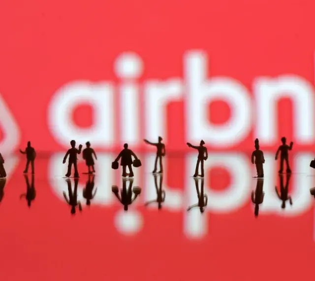 Małe figurki ludzi na tle logo Airbnb. Zastanawiasz się airbnb co to? To platforma do rezerwacji noclegów.