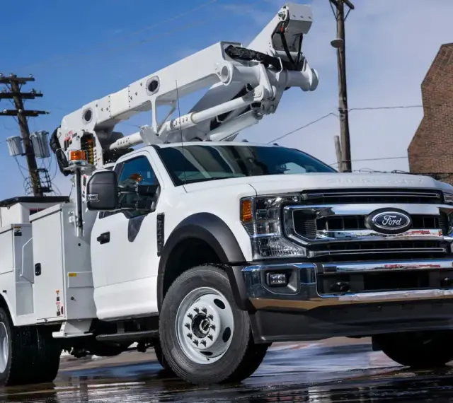 Biały Ford F650 z podnośnikiem koszowym gotowy do pracy przy liniach energetycznych.
