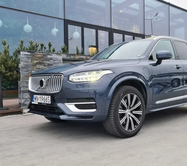 Elegancki, ciemnoszary Volvo XC90 T8 z nowoczesnymi światłami LED stoi przed budynkiem z dużymi, przeszklonymi oknami.
