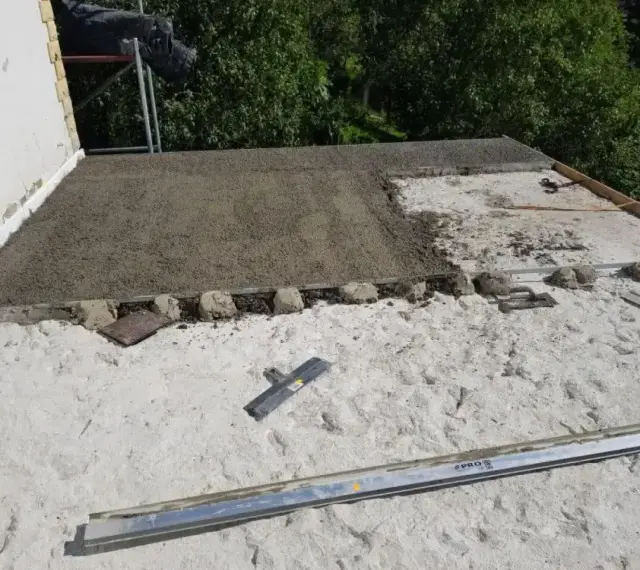 Budowa dachu płaskiego. Wylewanie warstwy styrobetonu, widoczne narzędzia i elementy konstrukcyjne. Prawidłowe proporcje styrobetonu kluczowe dla izolacji.