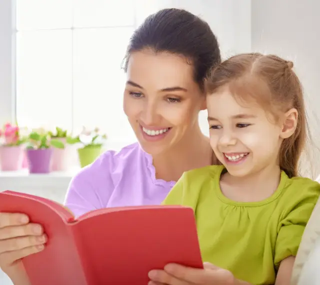 Uśmiechnięta mama czyta bajkę córce. To wspaniała opieka na dziecko 2 dni w tygodniu, pełna radości i wspólnych chwil.
