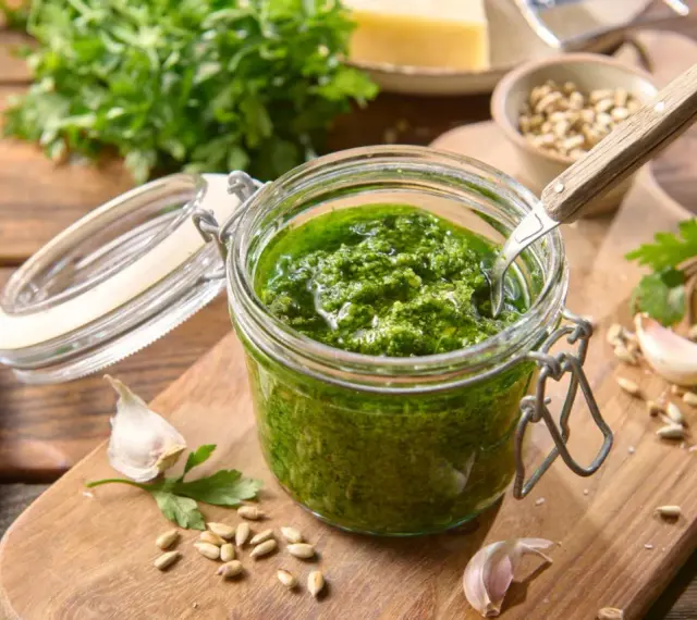 Słoik domowego pesto z pietruszki, z czosnkiem, nasionami słonecznika i serem w tle. Idealne do makaronu lub na grzanki.