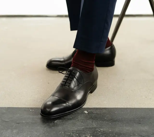 Eleganckie czarne buty męskie, rozmiar buta 50, z bordowymi skarpetkami i granatowymi spodniami.