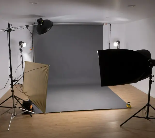 Studio fotograficzne z szarym tłem, lampami i dyfuzorem. Światło kontrowe tworzy dramatyczne cienie.