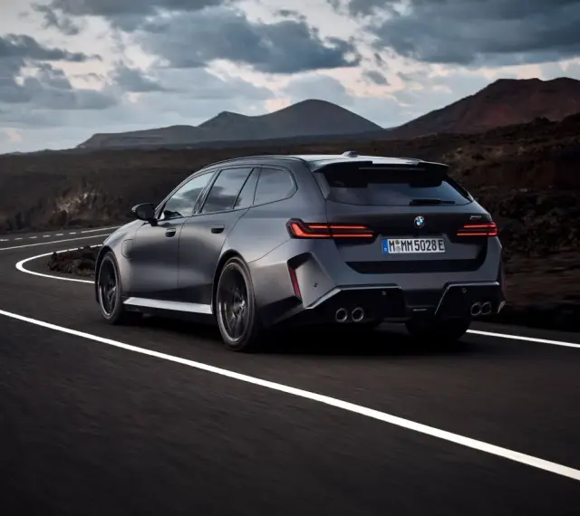 Mocne BMW M5 Touring pędzi po krętej drodze pośród surowego krajobrazu.