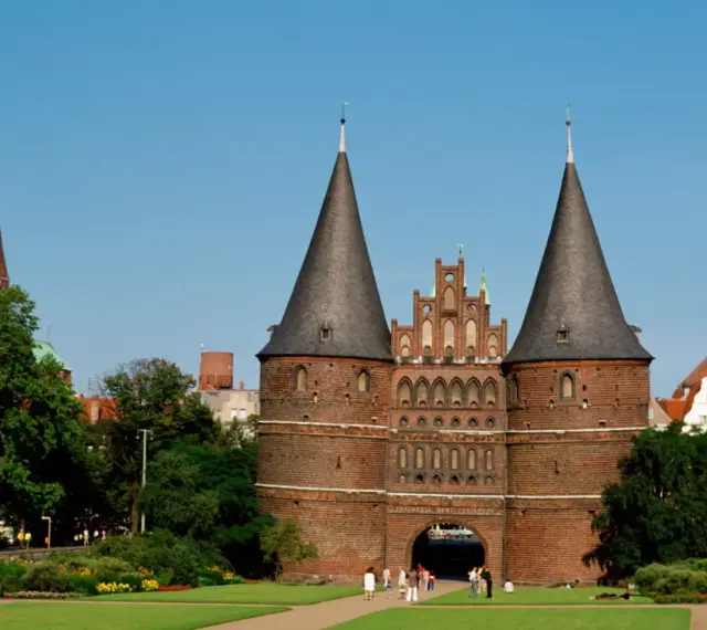 Holstentor in Lübeck, ein Wahrzeichen für Ihre **Ferien Schleswig-Holstein 2025**. Historische Backsteinarchitektur mit Türmen und grünen Parks.
