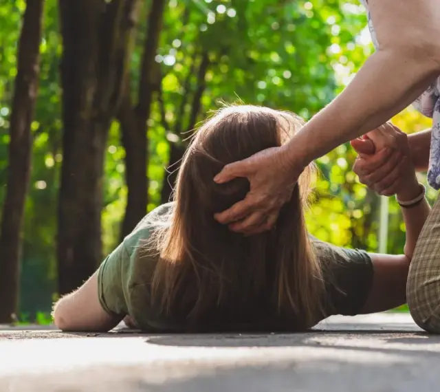 Osoba na ziemi, pomagająca jej druga osoba. Czy padaczka jest uleczalna? Ta scena budzi pytania o zdrowie i wsparcie.