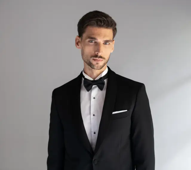 Elegancki mężczyzna w czarnym smokingu z białą poszetką. Dowiedz się, jak dobrać poszetkę do stylizacji.