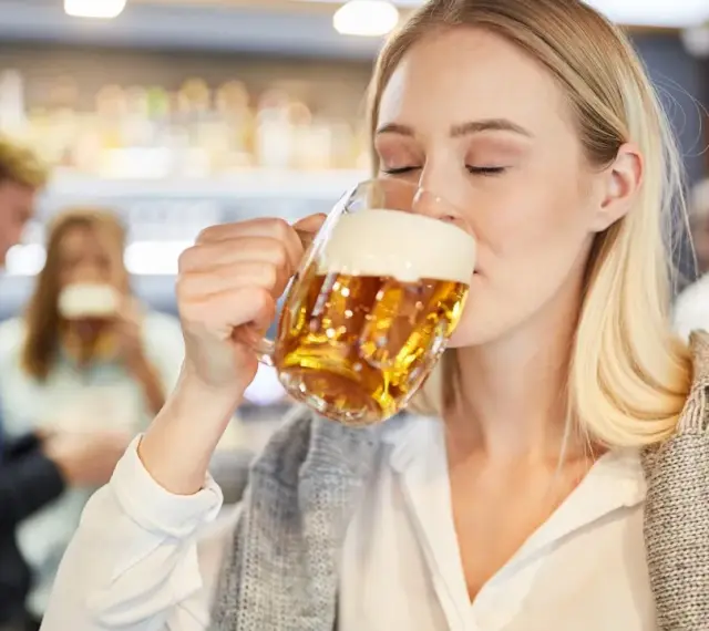 Kobieta z zamkniętymi oczami pije piwo bezalkoholowe w ciąży, ciesząc się smakiem w pubie.