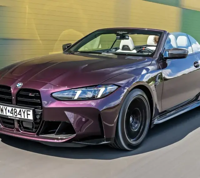 Fioletowe BMW M4 Competition kabriolet pędzi po drodze, odsłaniając białe wnętrze i sportowe detale.