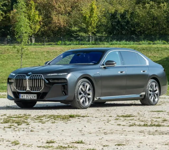 Elegancki, grafitowy BMW 740d na tle zieleni. Luksusowa limuzyna prezentuje się imponująco.