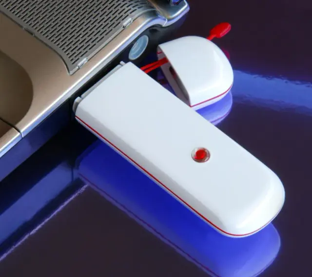 Biały modem USB podłączony do laptopa, umożliwiający komórkową transmisję danych.