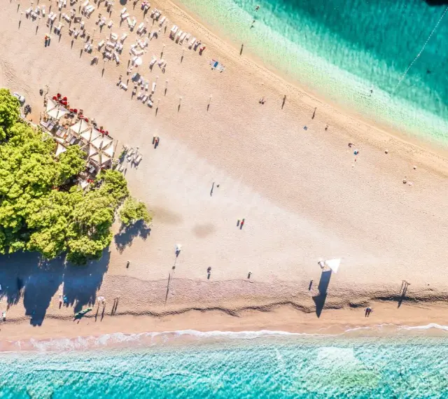 Chorwacja plaże piaszczyste, z turkusową wodą i zielonymi drzewami. Leżaki i parasole czekają na plażowiczów.