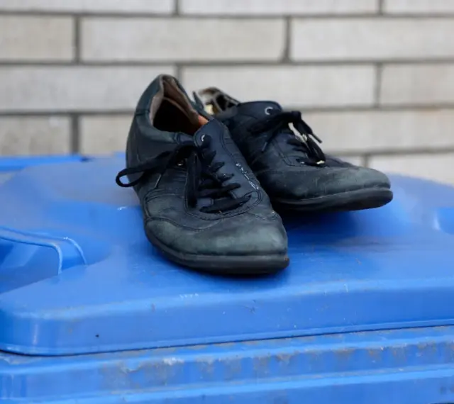 Stare, czarne buty leżą na niebieskim koszu na śmieci. Czas zastanowić się, gdzie wyrzucić stare buty, by dać im drugie życie.