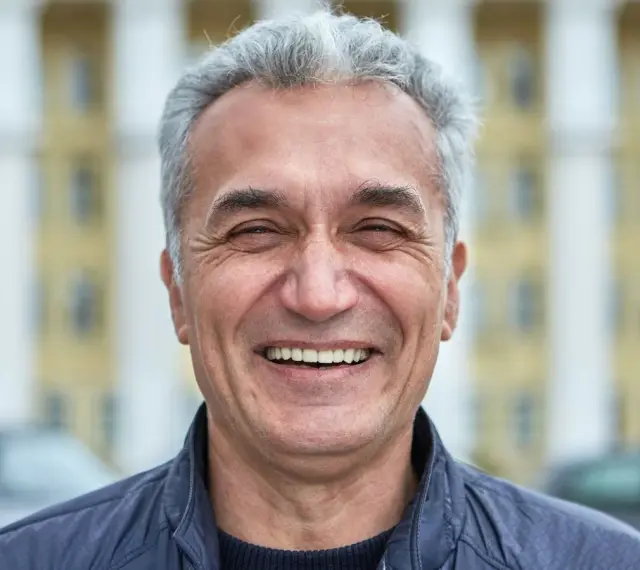 Uśmiechnięty mężczyzna z siwymi włosami, który wygląda jak typowy boomer. Co to znaczy? To ktoś z pokolenia wyżu demograficznego, często kojarzony z pewnymi wartościami i stylem życia.