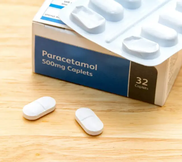 Opakowanie paracetamolu 500mg i dwie tabletki na drewnianym tle. Szybka ulga w bólu zęba.