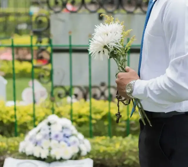Mężczyzna w białej koszuli i niebieskim krawacie trzyma bukiet białych kwiatów i różaniec. To jego urlop okolicznościowy śmierć teścia.