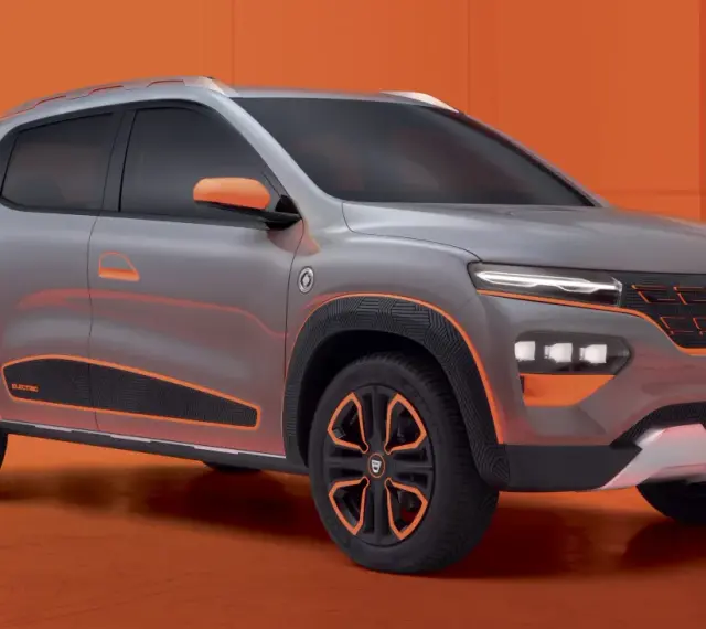 Szary samochód Dacia Spring z pomarańczowymi akcentami na tle pomarańczowym.