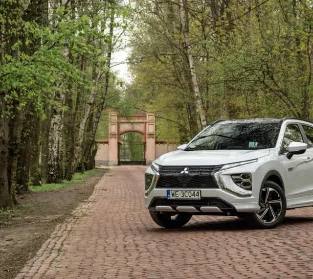 Biały Mitsubishi Eclipse Cross na tle bramy i drzew. Wiele pozytywnych mitsubishi eclipse cross opinie potwierdza jego wszechstronność.
