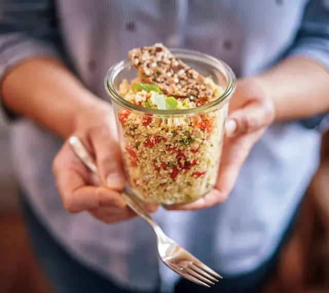 Un bocal rempli de quinoa coloré, parfait pour un régime sain. Une fourchette est prête à déguster ce plat savoureux.